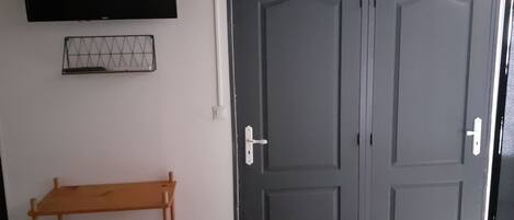 A room with a double door, a TV mounted on the wall, and a wooden shelf.