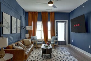 Een woonkamer met een bank, fauteuils, een salontafel, een televisie en een kamerkleed met een patroon.