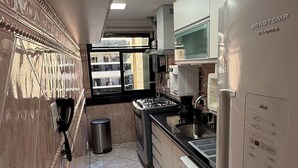 Ett modernt kök med ett kylskåp i rostfritt stål, en inbyggd ugn och en gasspis. Det finns ett fönster som släpper in naturligt ljus och ger utsikt över omgivningen.