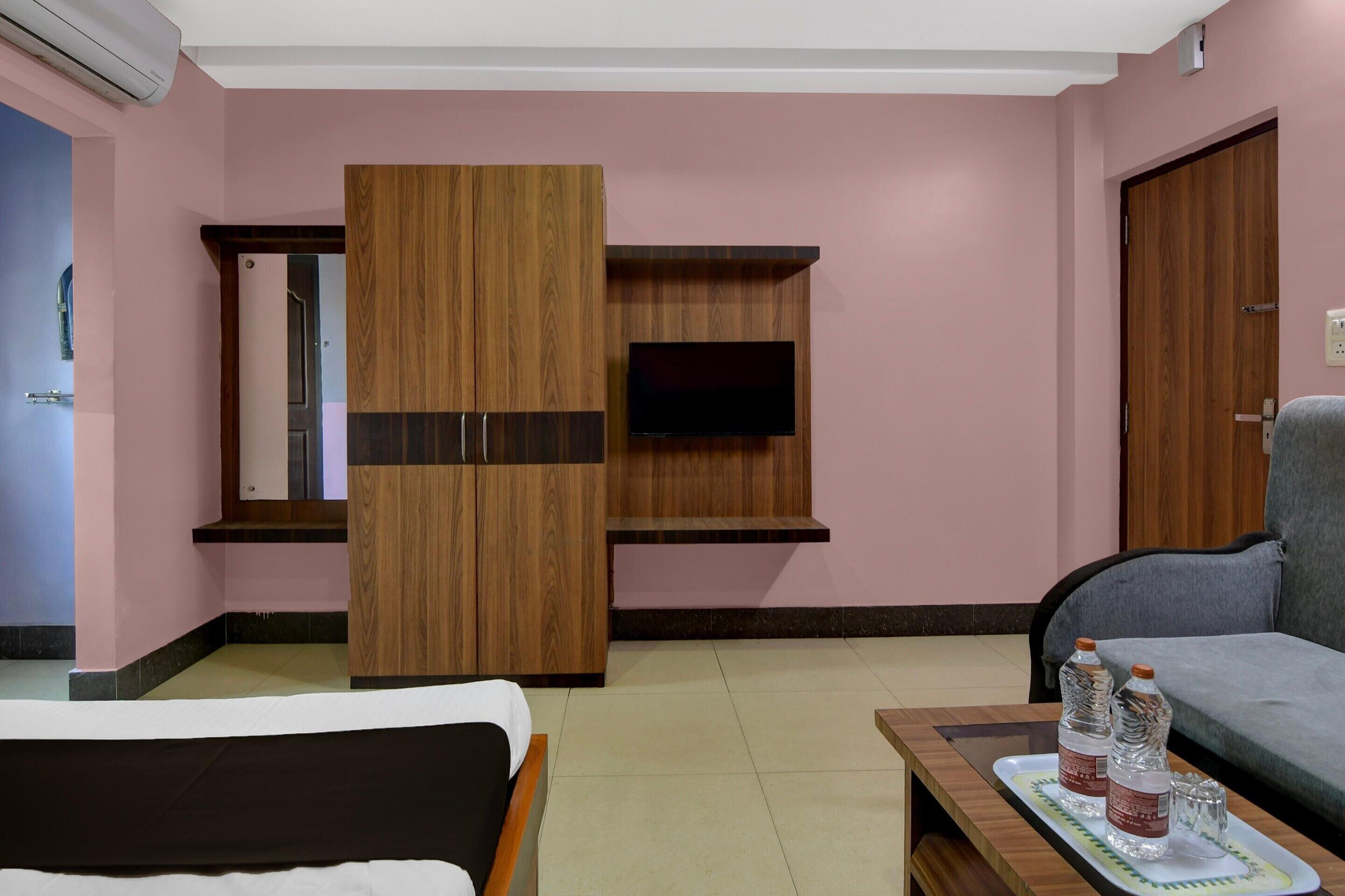 A hotel room with a bed, a sofa, a TV mounted on the wall, and a wooden wardrobe.