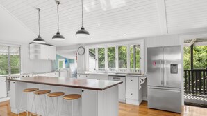 A modern kitchen with a large island, bar stools, stainless steel appliances, and large windows. - Relaxing Retreat With Outdoor Space in Fairfield (Brisbane)