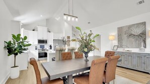 Una cocina moderna con armarios blancos, un microondas y un comedor con mesa de madera y sillas de cuero.