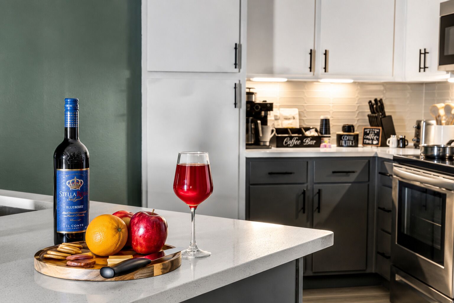 Una cocina moderna con una encimera, una botella de Stella Artois, una copa de vino tinto y frutas.