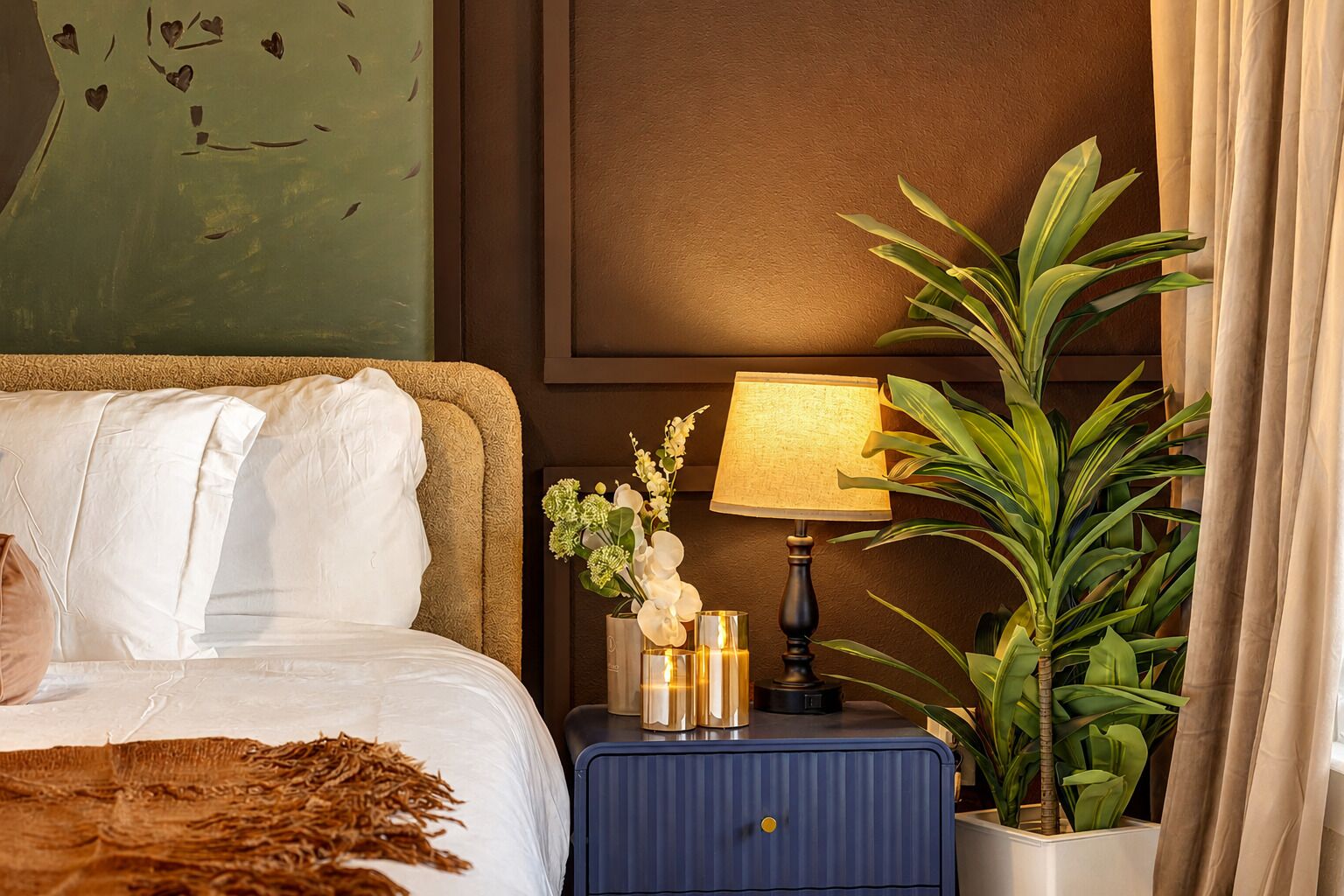 Ein Hotelzimmer mit Bett, Nachttisch mit Lampe, Blumen in einer Vase und einer Topfpflanze.