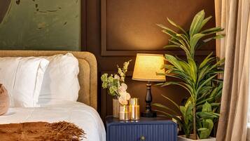 Ein Hotelzimmer mit Bett, Nachttisch mit Lampe, Blumen in einer Vase und einer Topfpflanze.