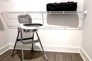 A baby high chair with a tray table, a black bag on a shelf, and a white radiator in the background. - Resort-Style suite near Universal (Frisco)