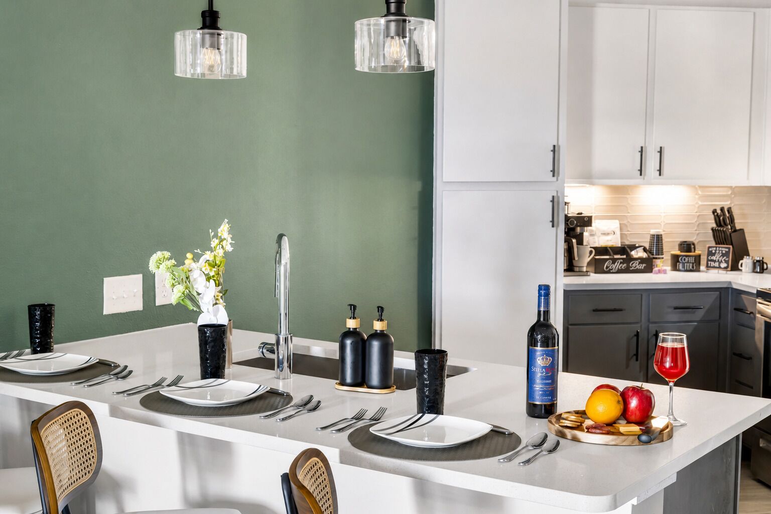 Una cocina moderna con una isla central, armarios blancos y una pared verde de acento.
