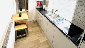 A compact kitchen with a black countertop, white cabinets, a built-in stove, and a window with blinds. - Studio 4@Bransford Rd (Worcester)