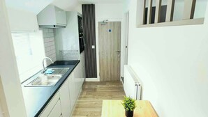A narrow kitchen with a wooden table and a potted plant, white cabinets, and a black countertop. - Studio 4@Bransford Rd (Worcester)