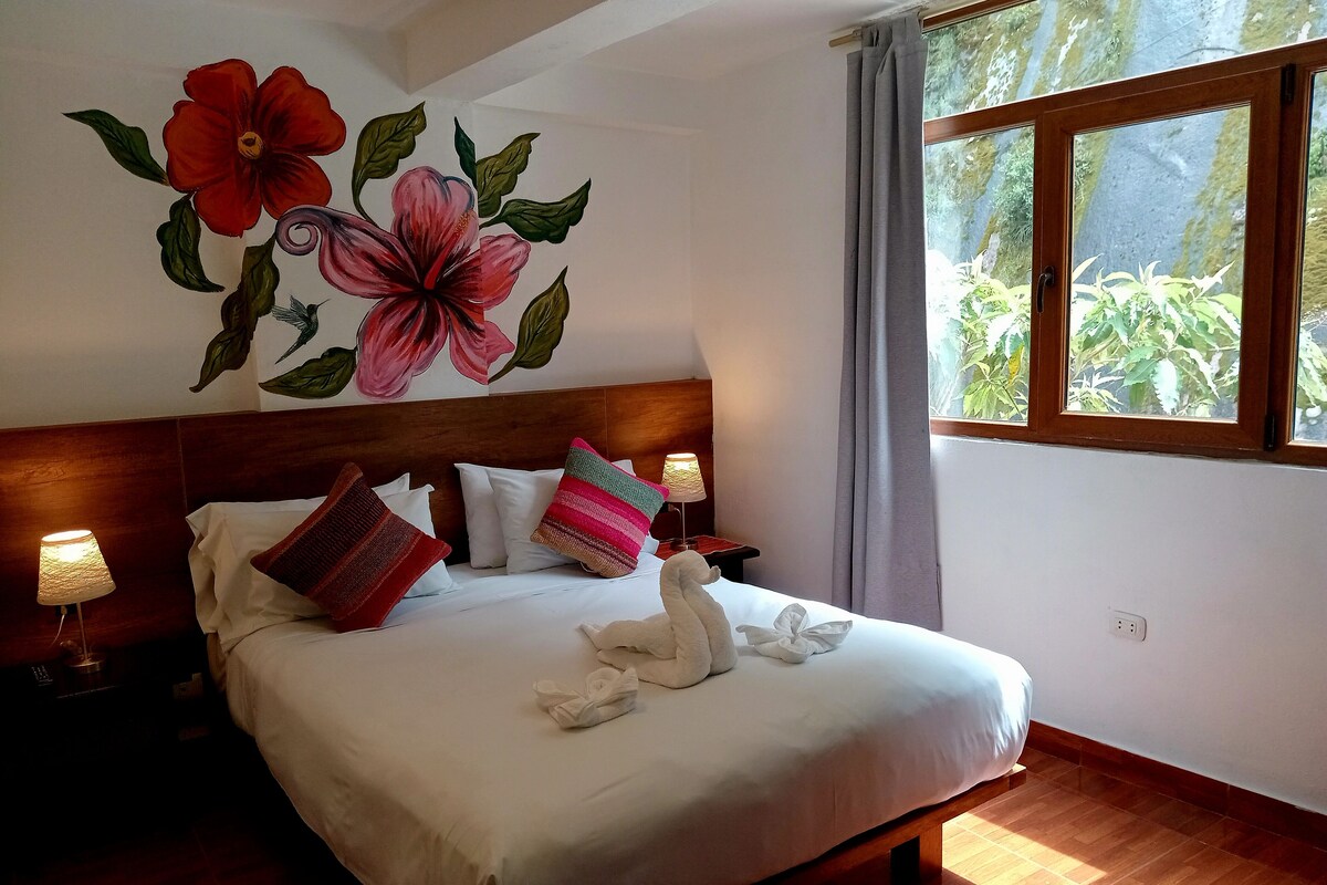 A neatly made bed with white linens and decorative pillows, a wooden headboard, and a wall mural of flowers.