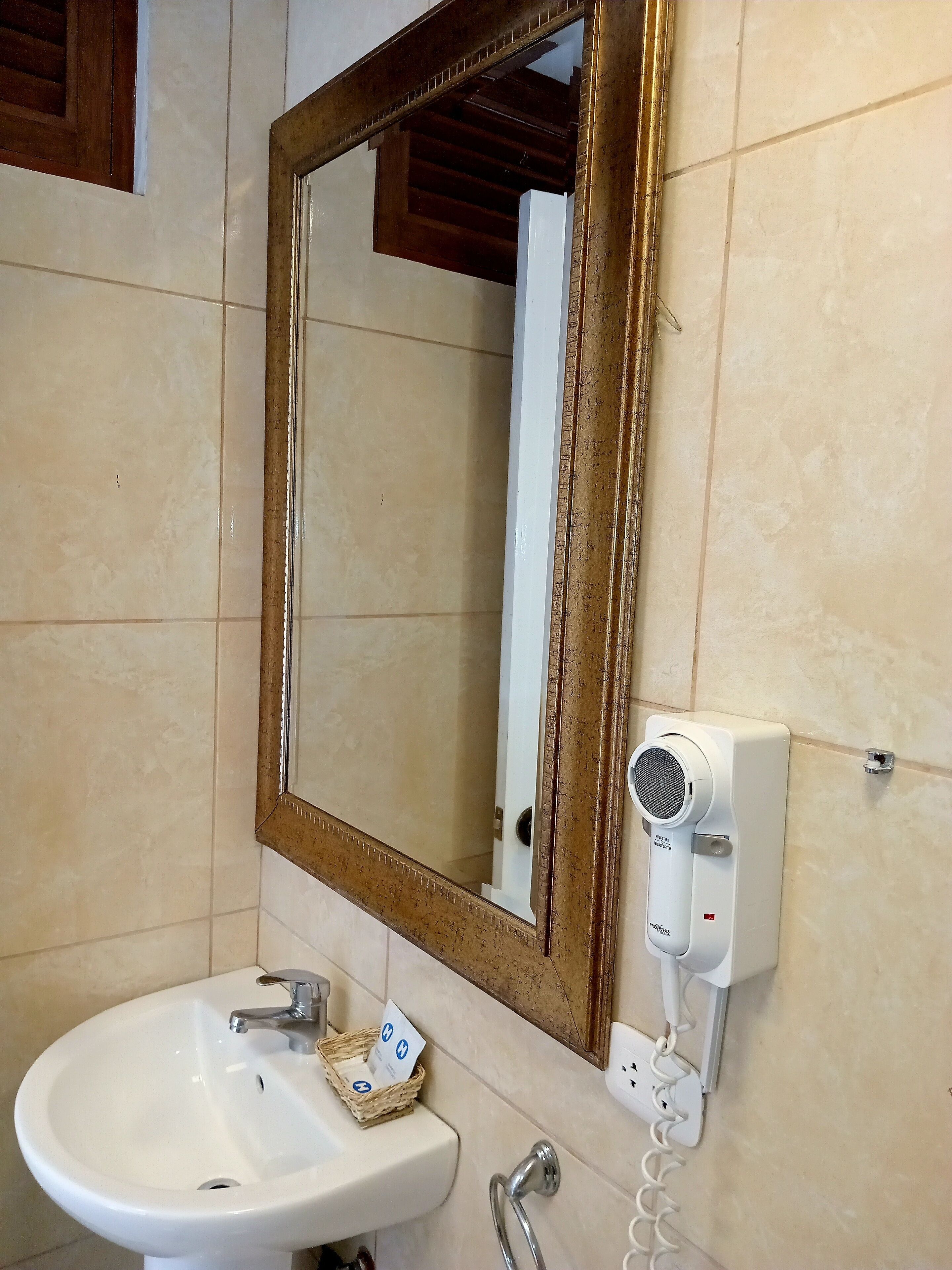 A bathroom with a white sink, a mirror with a wooden frame, and a hairdryer mounted on the wall.