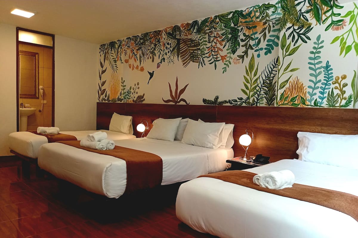 Ein Hotelzimmer mit drei Betten, einem Holzkopfteil, einem Wandgemälde und einer Nachttischlampe.