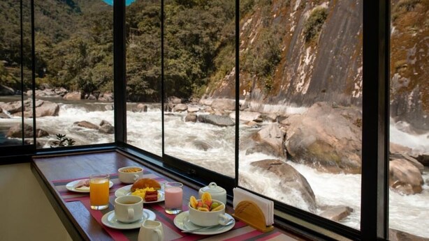 Een ontbijttafel met diverse gerechten en een uitzicht op een rivier en bergen door grote ramen.