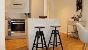 A modern kitchen with a built-in oven, two bar stools, a white island, and a metal cart with bottles. - Comfortable living in the center - elevator and barrier-free (Detmold)