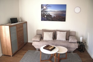 A living room with a sofa, a chessboard, a desk with a laptop, and a painting on the wall. - Landhaus am See - Apartment Reiherbachtal, directly on Lake Edersee (Waldeck)
