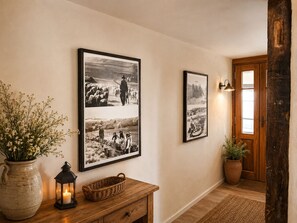 Un passadís amb terra de fusta, un ram de flors, una espelma, un farol i dos fotografies en blanc i negre emmarcades a la paret.