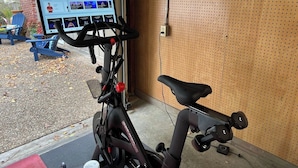 A stationary bike with a digital display, a wall-mounted pegboard, and a blue chair outside. - Executive King Bungalow on Mount Sequoyah (Fayetteville)