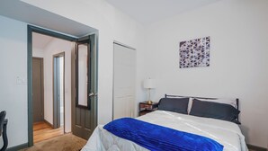 A bedroom with a bed, a nightstand, a lamp, and a door leading to another room. - Stylish & Quiet 3BD Sleeps 8 / Near Stadium & DT (Jacksonville)