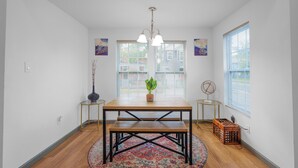 A dining area with a wooden table, bench, and a potted plant. There are two side tables with lamps, a decorative rug, and a window with blinds. - Stylish & Quiet 3BD Sleeps 8 / Near Stadium & DT (Jacksonville)