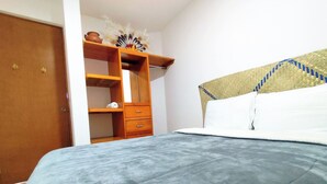 A bedroom with a bed, a wooden wardrobe, and a shelf with decorative items. - Apartment in the heart of Oaxaca (Oaxaca de Juárez)