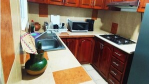 A kitchen with wooden cabinets, a microwave, a stove, and a sink. - Apartment in the heart of Oaxaca (Oaxaca de Juárez)