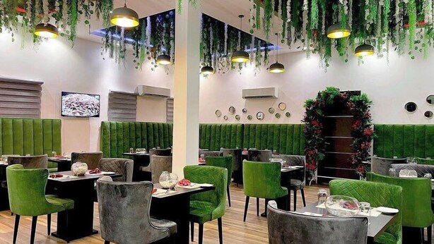 A restaurant with green upholstered booths, round tables, and hanging plants. - Chatkrum Hotel (Abuja)