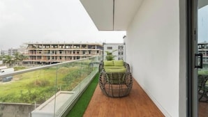 A balcony with a wicker chair, a glass railing, and a view of a building under construction. - Chatkrum Hotel (Abuja)