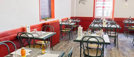 L’intérieur d’un restaurant, avec de nombreuses tables et chaises, un menu écrit à la craie et une fenêtre ornée de rideaux.