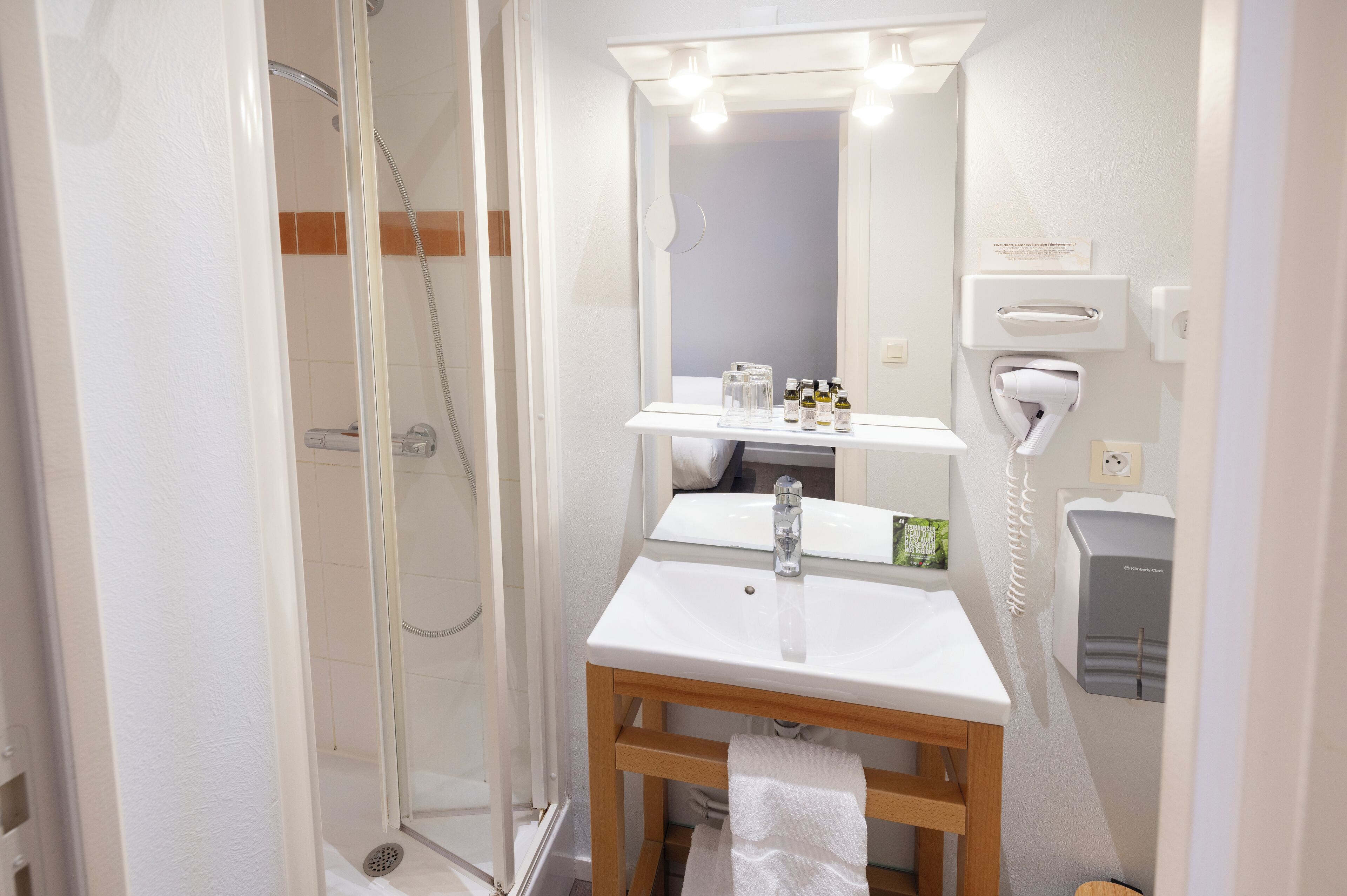 Ein modernes Badezimmer mit einer Duschkabine aus Glas, einem weißen Waschbecken mit Holzunterschrank und einem Spiegel mit Beleuchtung darüber.
