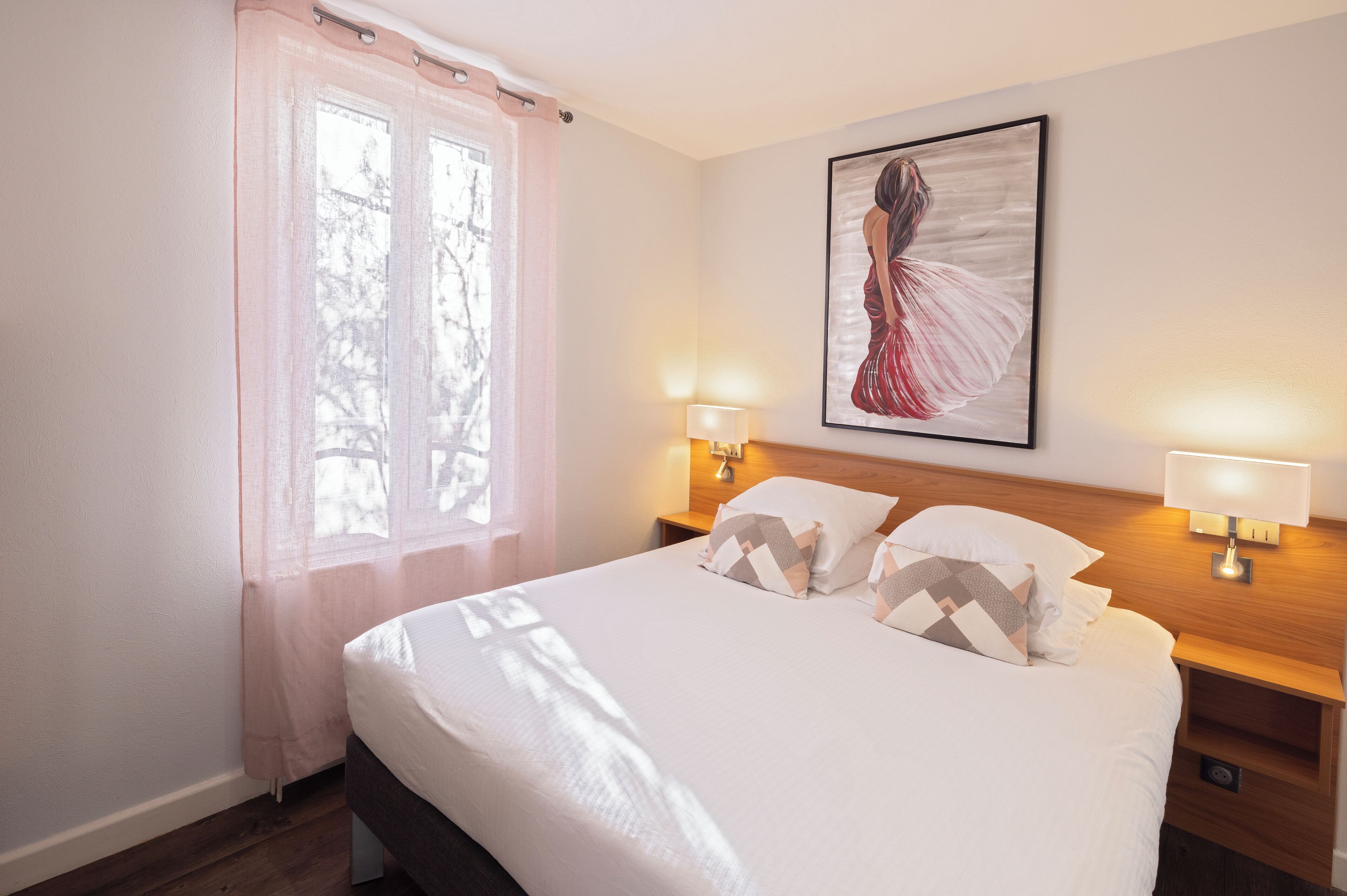 Een net opgemaakt bed met gestreepte kussens, een bedlampje en een ingelijst kunstwerk aan de muur.