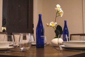 Ein Esstisch, gedeckt mit Tellern, Gläsern und blauen Flaschen, mit weißen Blumen im Hintergrund.