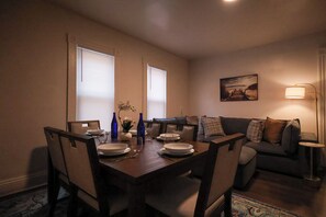 A dining area with a table set for four, a sofa, and a lamp. - The Weyl Collective 6BR Professional Retreat Near Downtown Rochester (Rochester)