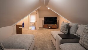 Et hyggeligt loftsværelse med et fladskærms-tv, grå sofaer og et lille bord.