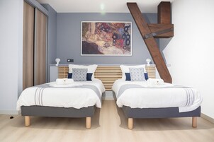 Une chambre moderne avec deux lits, une tête de lit en bois, une grande peinture abstraite et un plafond en pente.