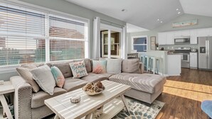 Een moderne woonkamer met een hoekbank, een eettafel en een keuken met witte kasten en roestvrijstalen apparatuur.