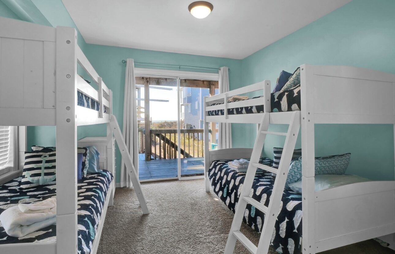 A room with bunk beds, a view of the outside, and a staircase leading to a balcony.