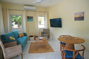 A living room with a sofa, a coffee table, a TV, and a dining area with chairs.