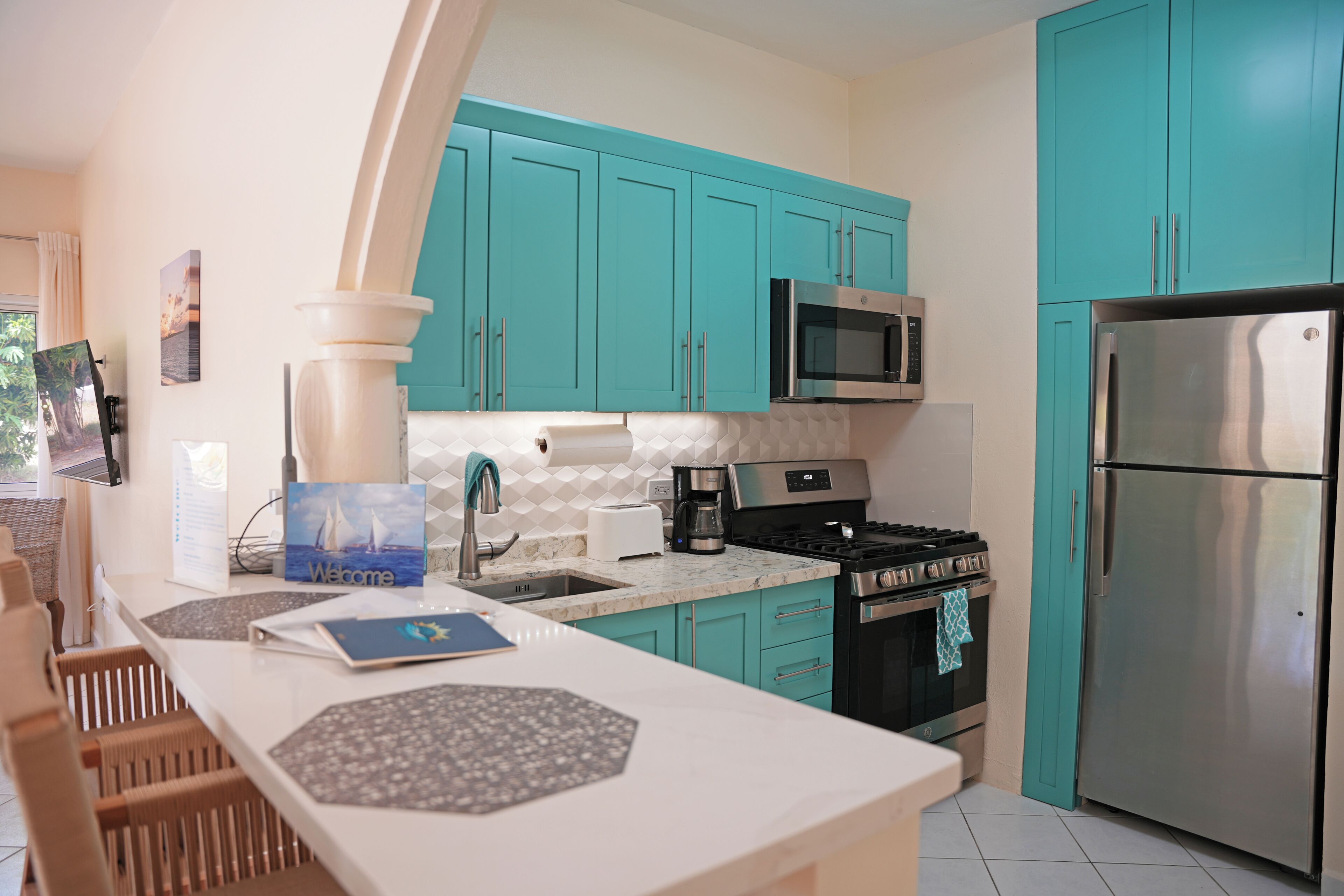 Una cocina moderna con armarios color turquesa, un refrigerador de acero inoxidable, un microondas y una estufa a gas.