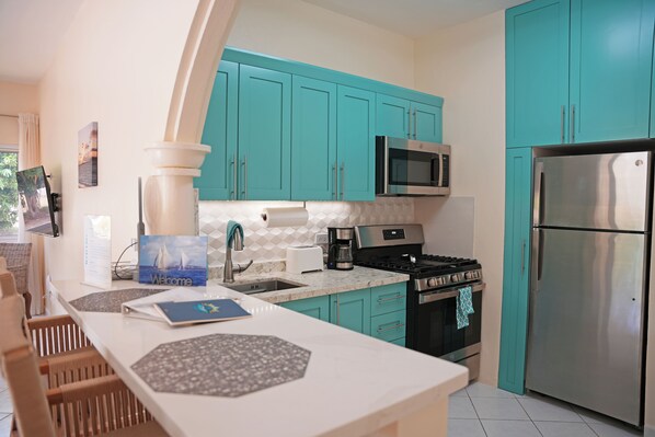 A modern kitchen with teal cabinets, a stainless steel refrigerator, a microwave, and a gas stove.