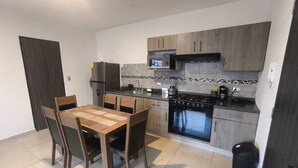 A modern kitchen with a dining table and chairs, a refrigerator, stove, microwave, and tiled backsplash. - Modern and centrally located apartment in CDMX (Ciudad de México)