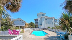 A residential area with a swimming pool, outdoor seating, and houses in the background. - Oceanview/Elevator/Pool/Hot tub/Steps to beach (Rodanthe)