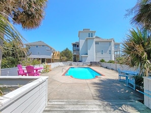 A residential area with a swimming pool, outdoor seating, and houses in the background.