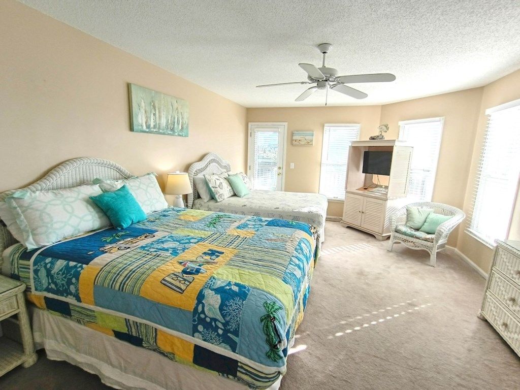 Quarto com cama grande, uma cadeira, televisão e ventilador de teto.