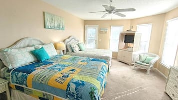 Quarto com cama grande, uma cadeira, televisão e ventilador de teto.