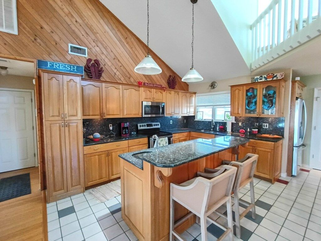 A kitchen with wooden cabinets, a granite countertop, a central island with bar stools, and a sign that reads 'FRESH.'