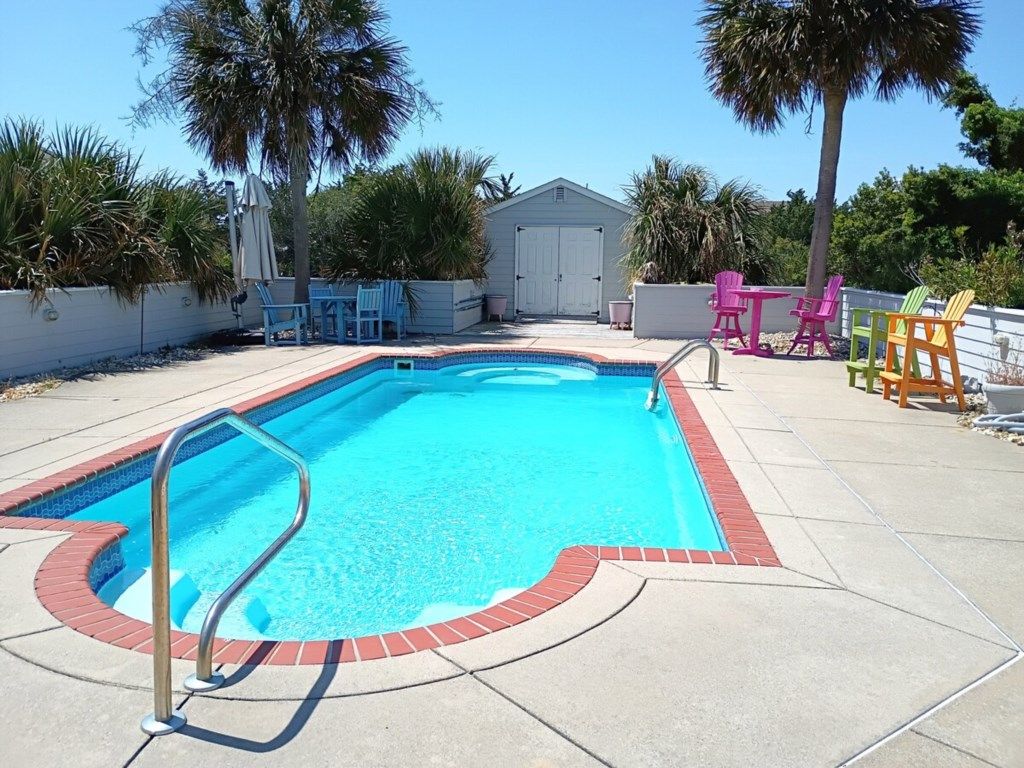 Una piscina rectangular con una escalera metálica, rodeada por una solana de hormigón.