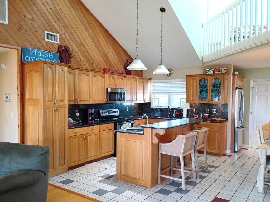 A kitchen with wooden cabinets, a central island with bar stools, a microwave, and a sign indicating fresh oysters.
