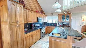 Eine Küche mit Holzausstattung, einer Granit Arbeitsplatte, einer Mikrowelle und einer großen Kochinsel mit Spüle.