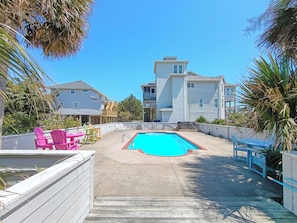 A residential area with a swimming pool, patio furniture, and houses in the background. - Oceanview 4Br w/elevator, private pool, hot tub, steps to beach access (Rodanthe)