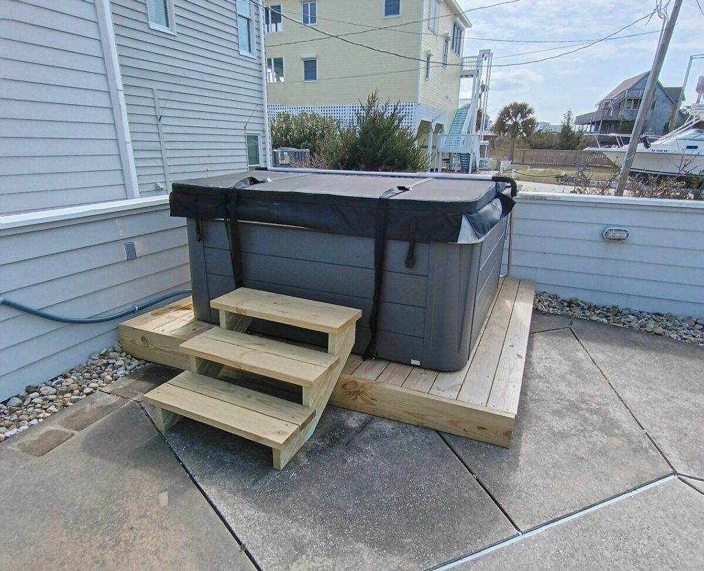 Un jacuzzi en una plataforma de madera con escalones que llevan a él, con vistas a un entorno residencial.